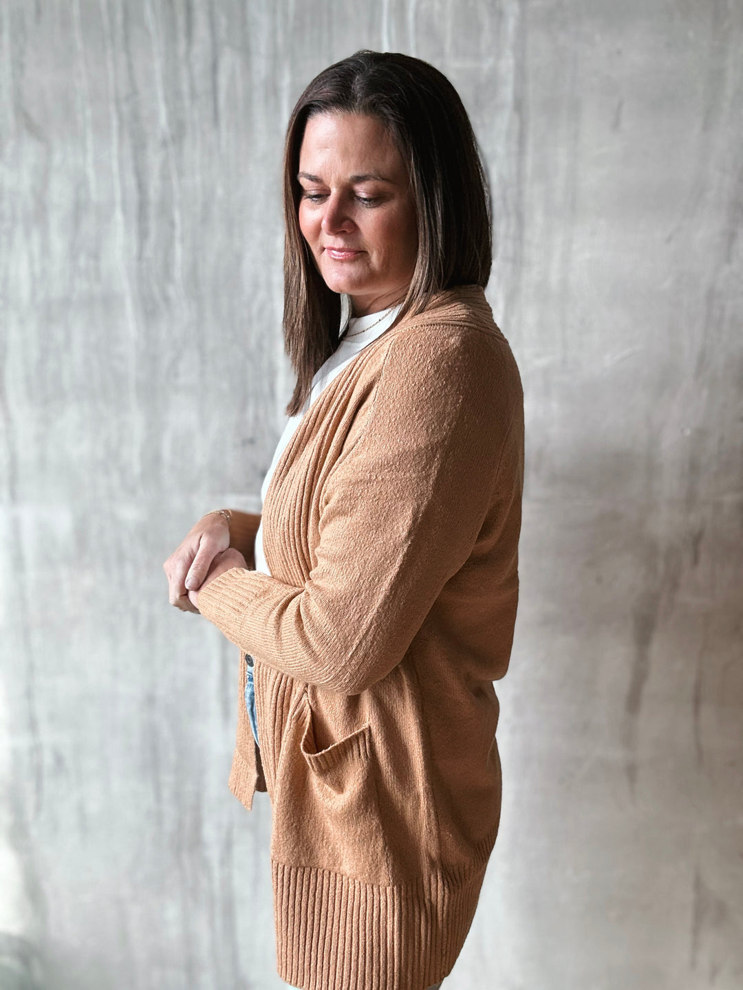 Woman wearing a beige cardigan against a textured white wall