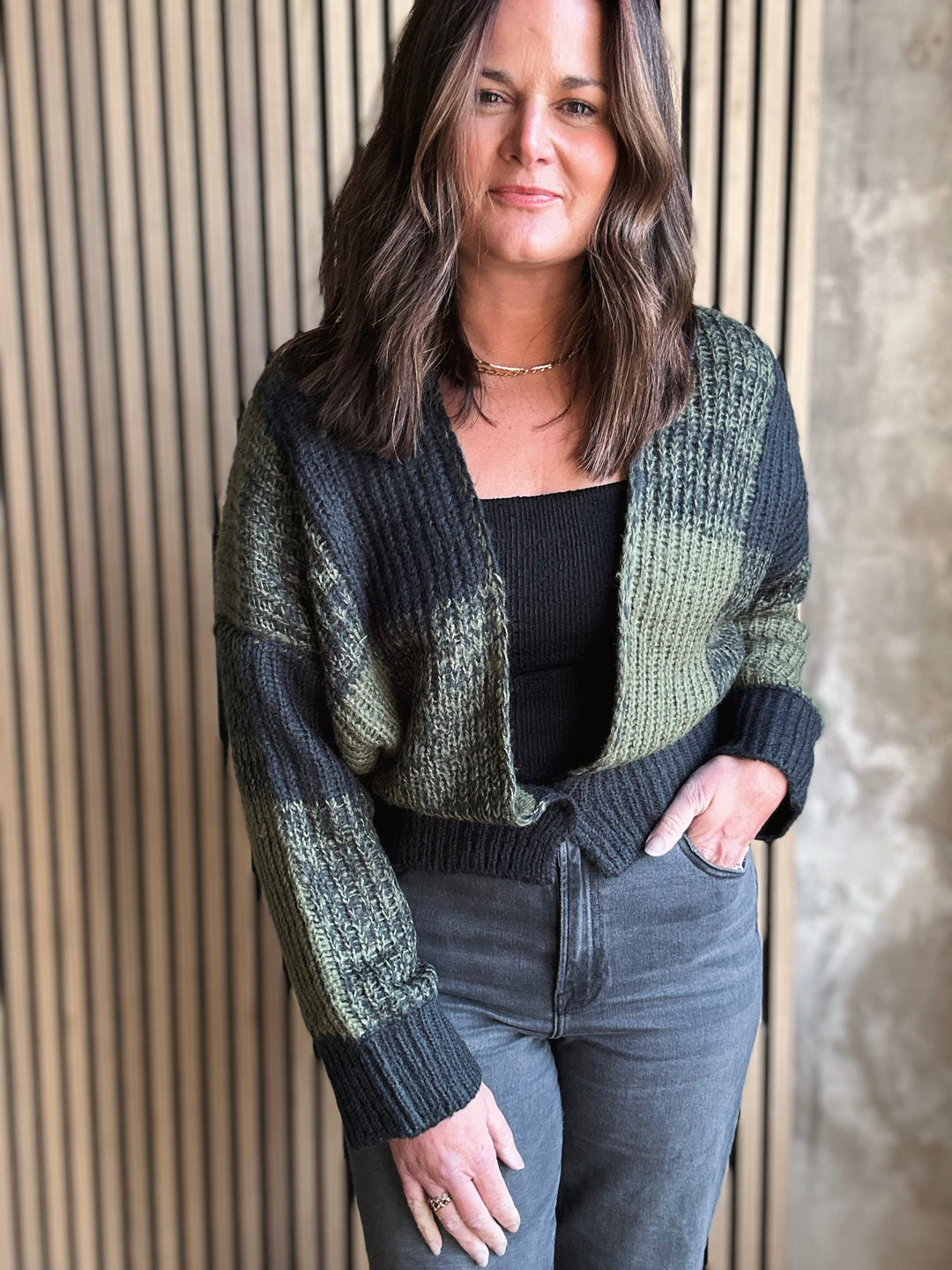 Woman wearing a green and black checkered cardigan against a textured wall.