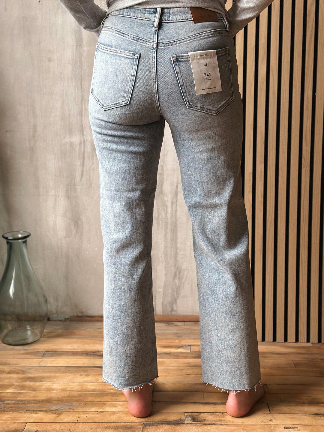 Person wearing light blue jeans standing in a room with wooden floor and neutral wall.