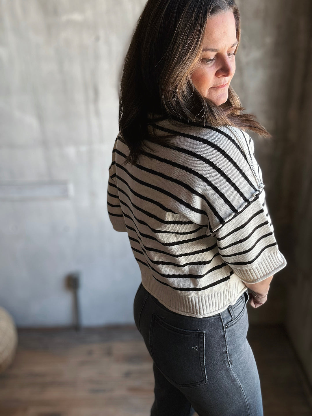 Woman wearing a striped sweater and dark jeans in a room with a textured wall.