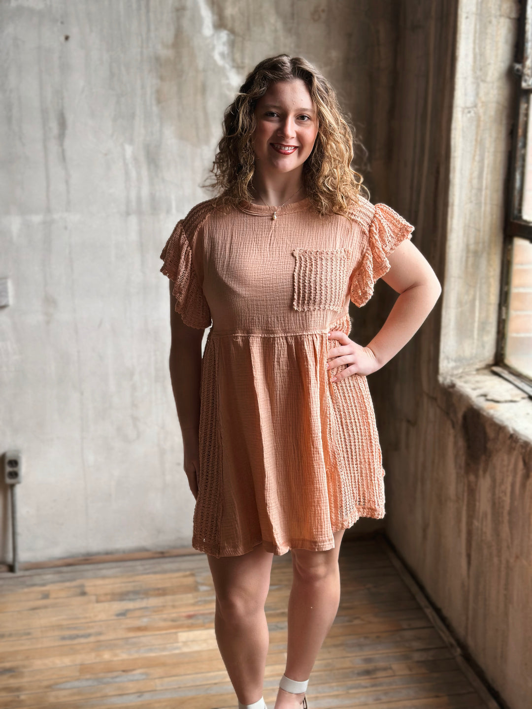 Woman in a peach dress standing in a room with concrete walls and wooden floor.