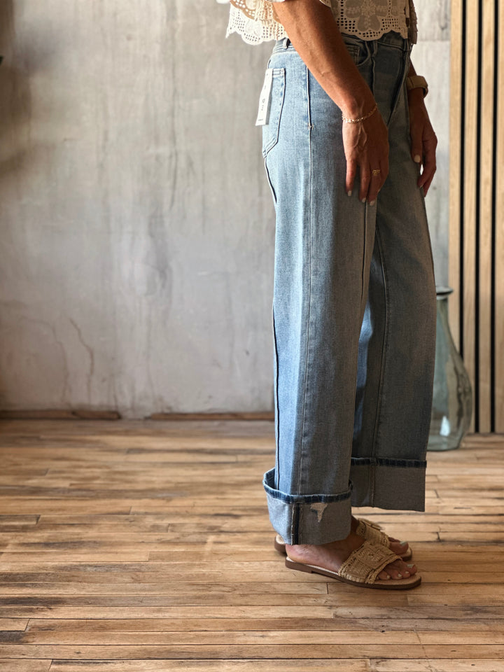Person wearing light blue jeans and sandals on a wooden floor with a neutral wall background