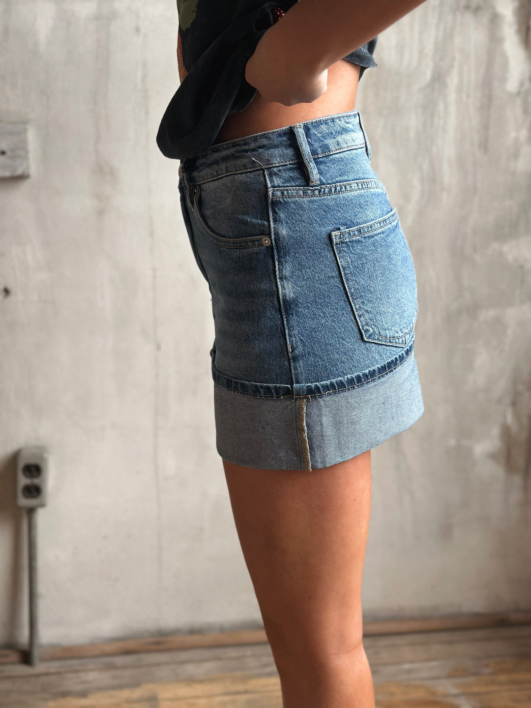 Person wearing a denim skirt against a neutral wall.