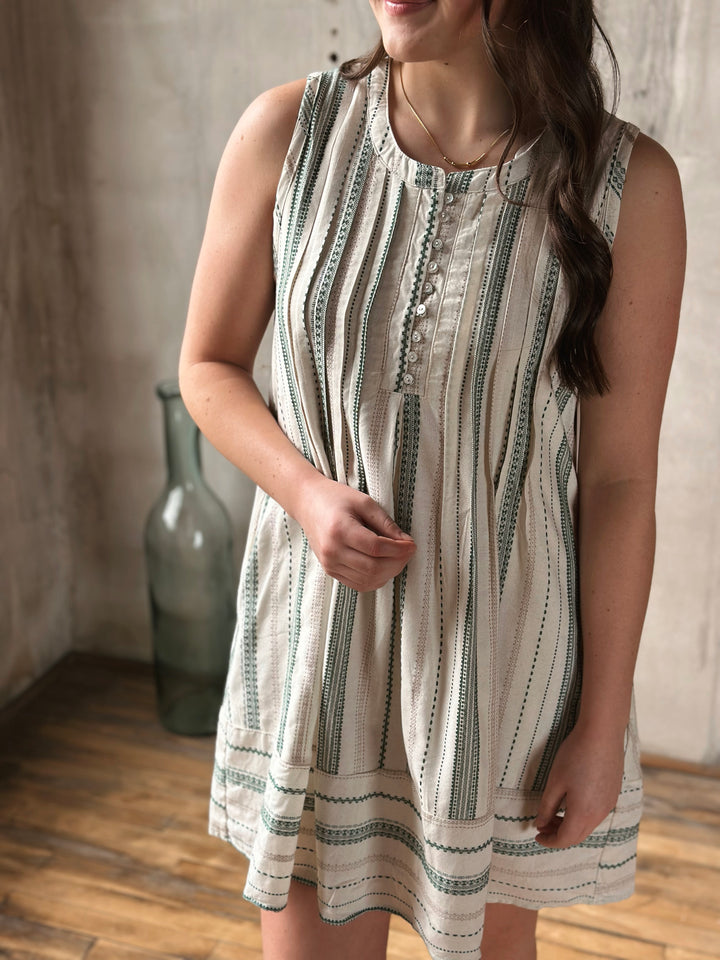 Woman wearing a sleeveless dress with a striped pattern in a room with a vase in the background.
