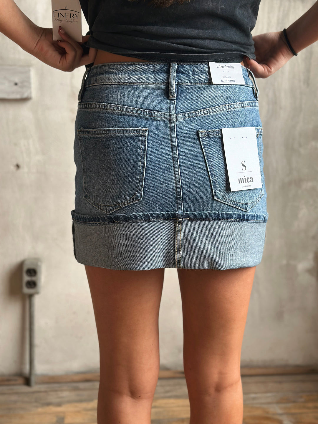 A person wearing a denim skirt standing against a neutral background.