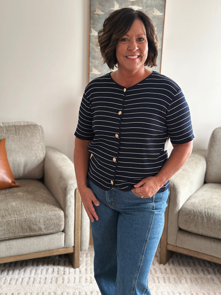 Woman wearing a navy striped shirt and jeans standing in a living room.