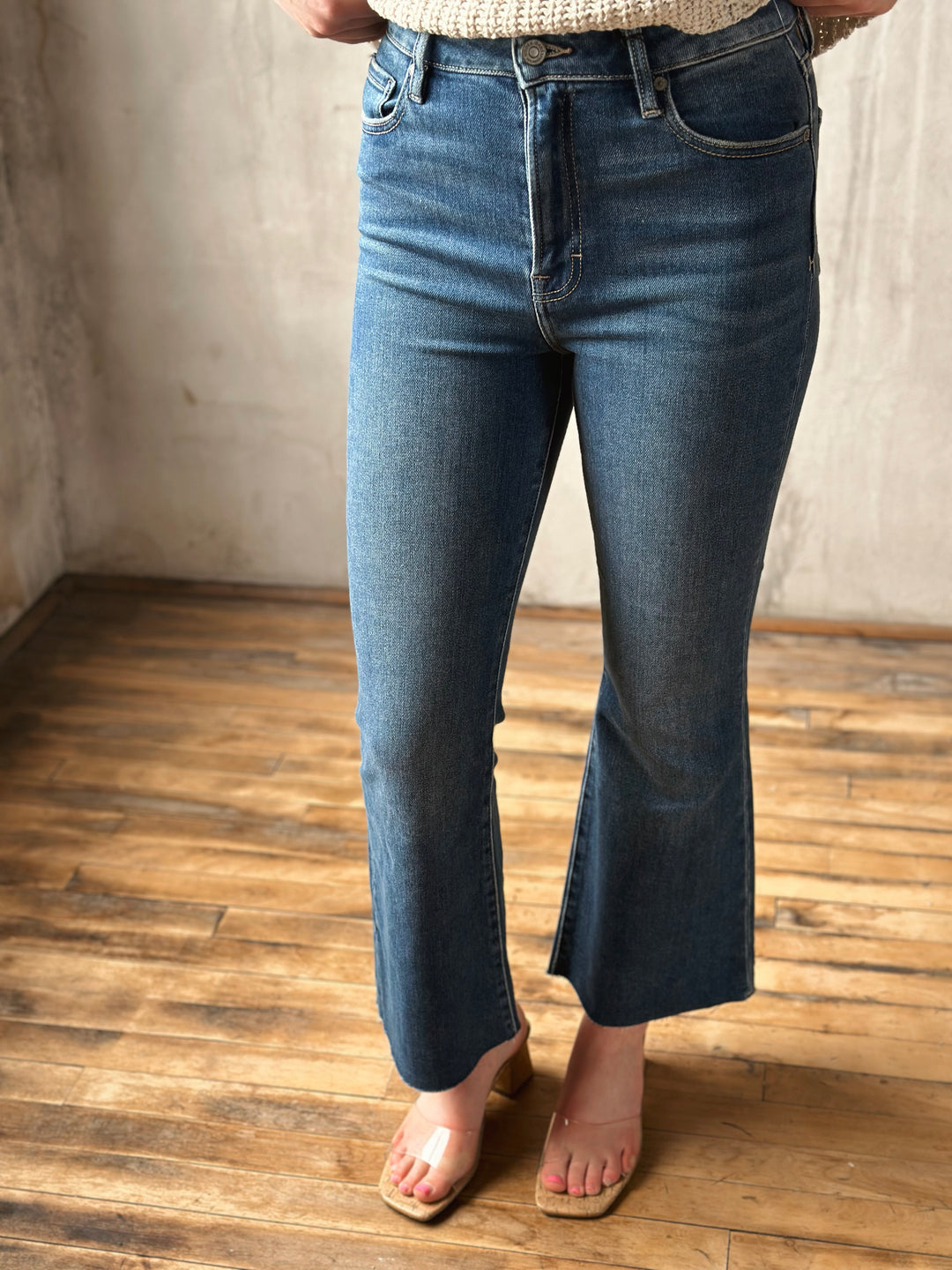 Person wearing blue jeans standing on a wooden floor with a neutral wall background
