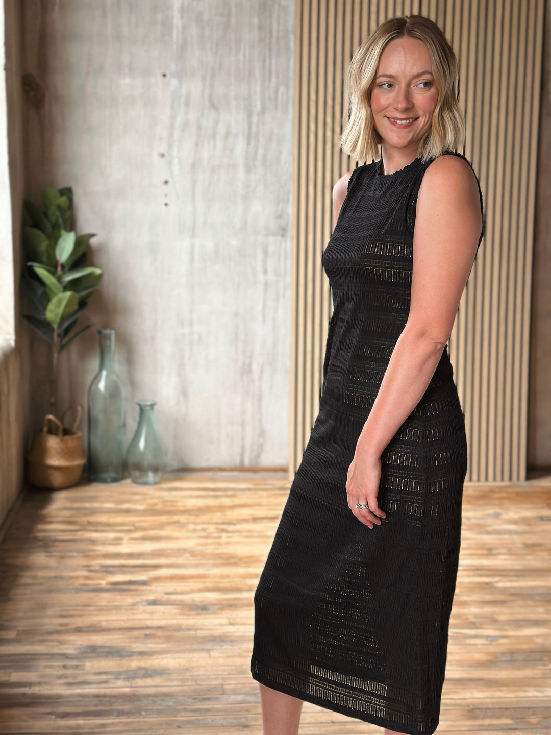 Woman wearing a black dress standing in a room with wooden flooring and decorative elements.