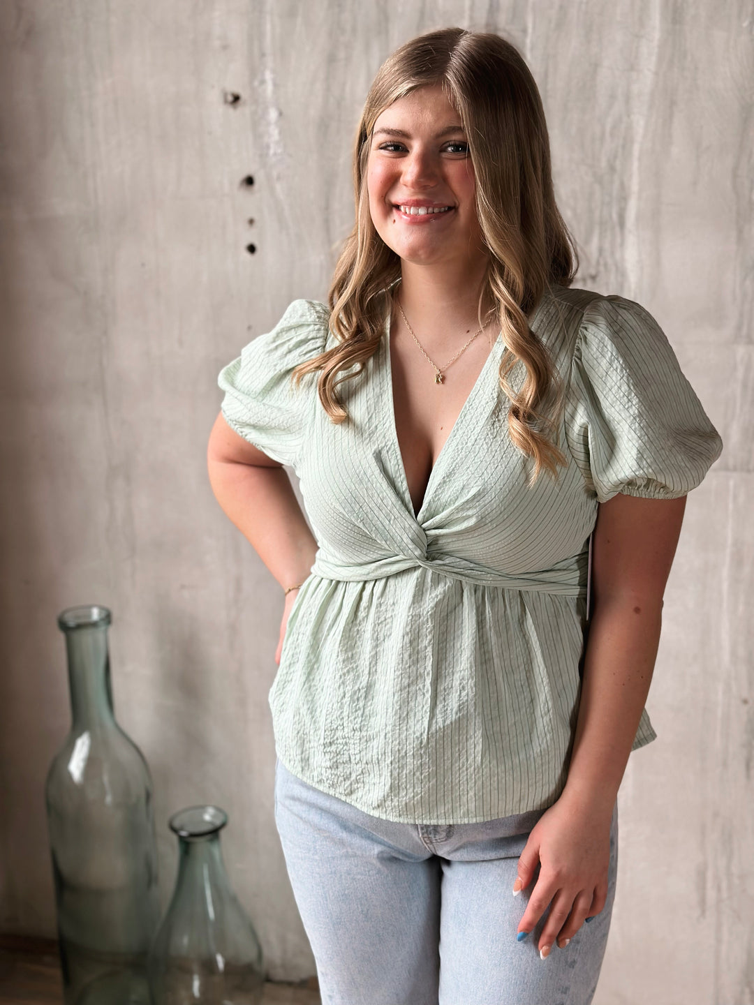 Woman wearing a light green top with puffed sleeves against a textured wall.