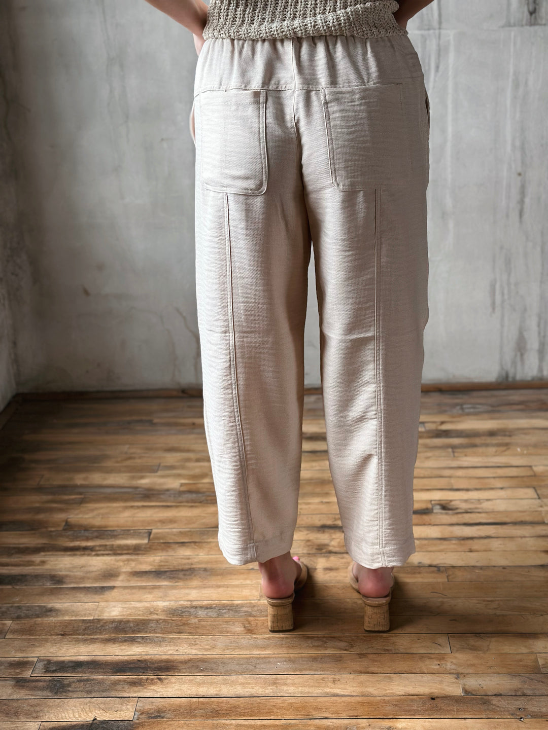 Person wearing beige pants standing on a wooden floor with a gray wall background