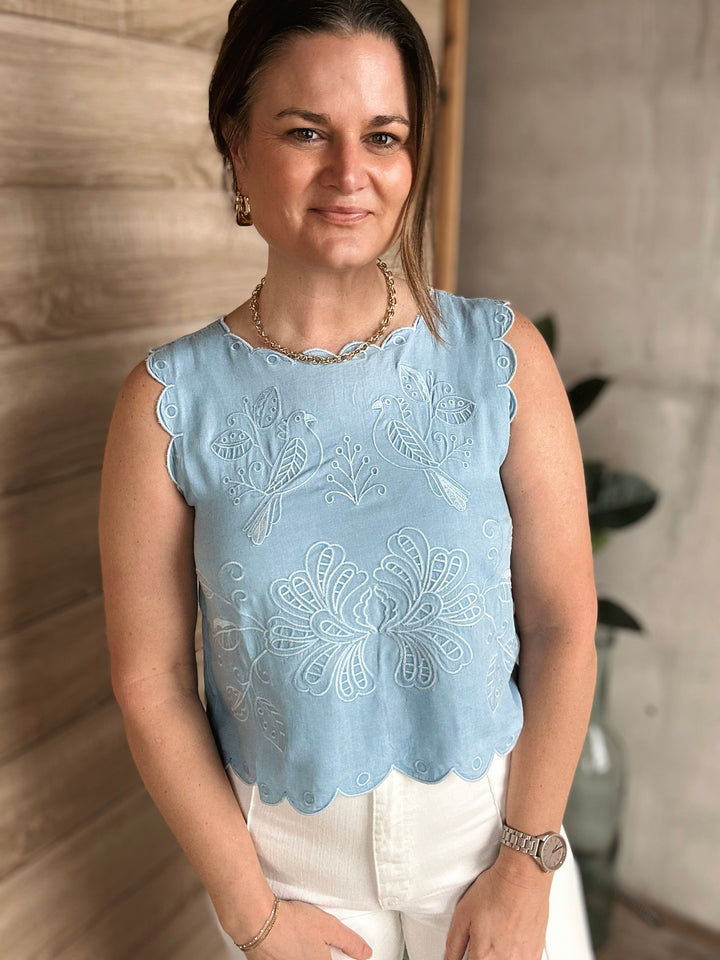 Woman wearing a light blue blouse with floral embroidery against a neutral background.
