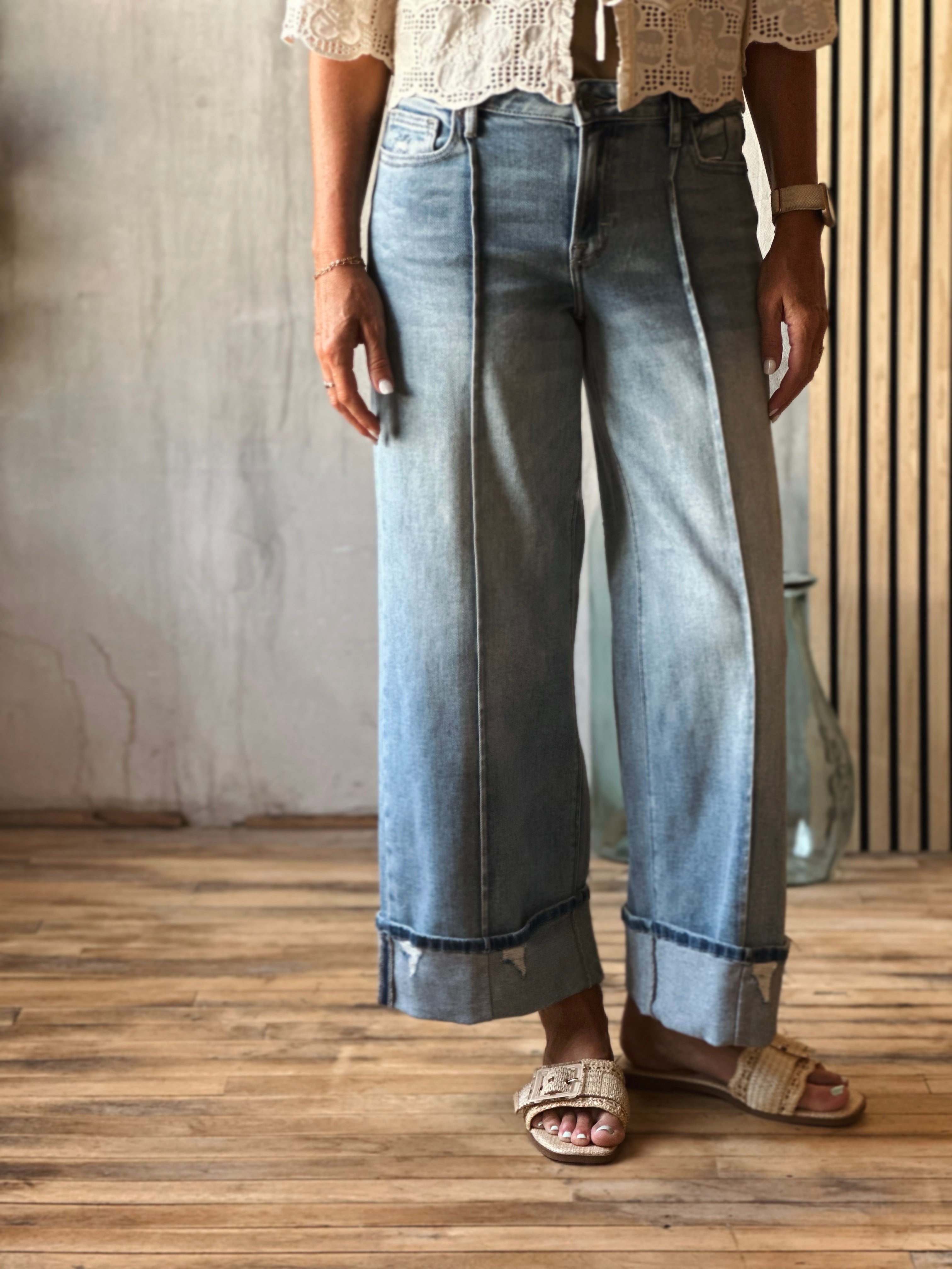 Person wearing light blue jeans and a white lace top on a wooden floor.