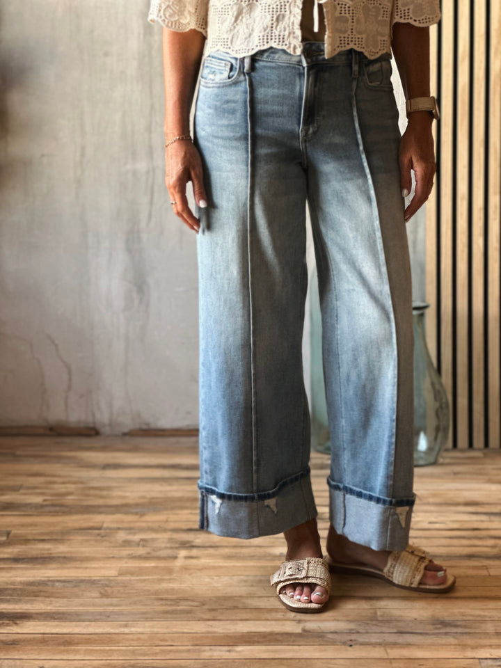 Person wearing light blue jeans and a white lace top on a wooden floor.