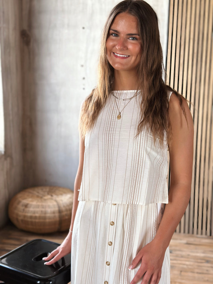 Woman wearing a white and beige sleeveless top with vertical stripes.