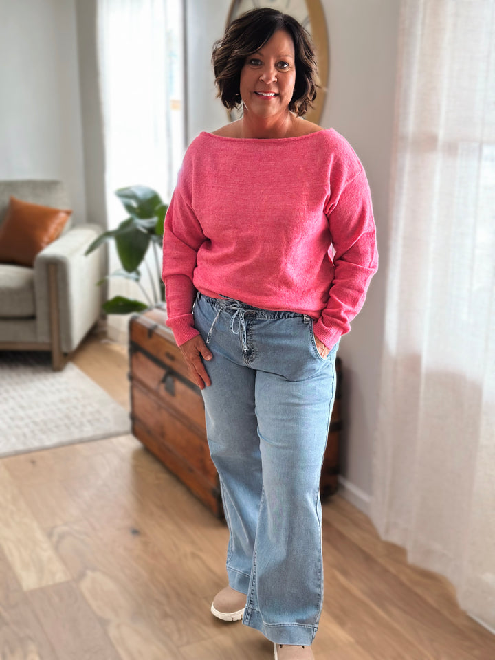 Woman wearing a pink sweater and blue jeans standing in a living room.