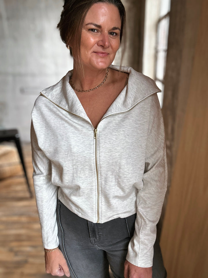 Woman wearing a light gray zip-up hoodie indoors with a neutral background