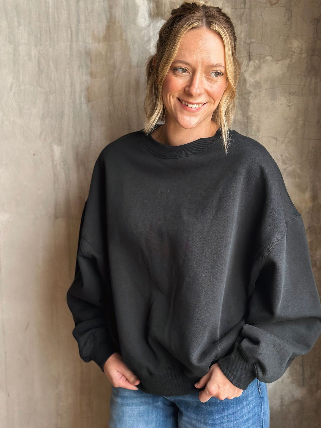 Person wearing a black sweatshirt against a textured wall