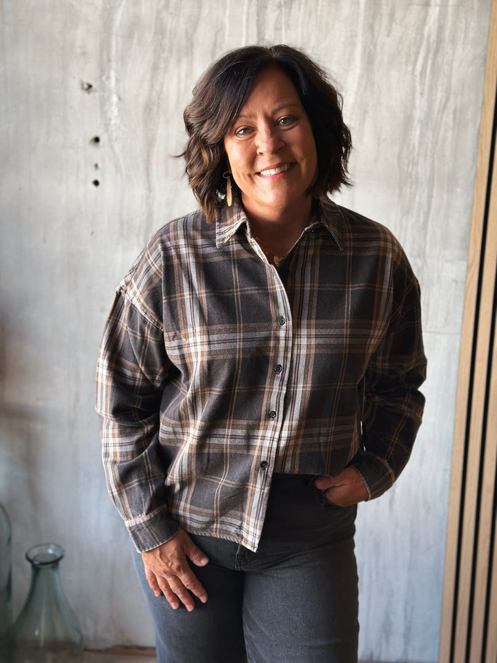 Woman wearing a plaid shirt standing against a textured wall.