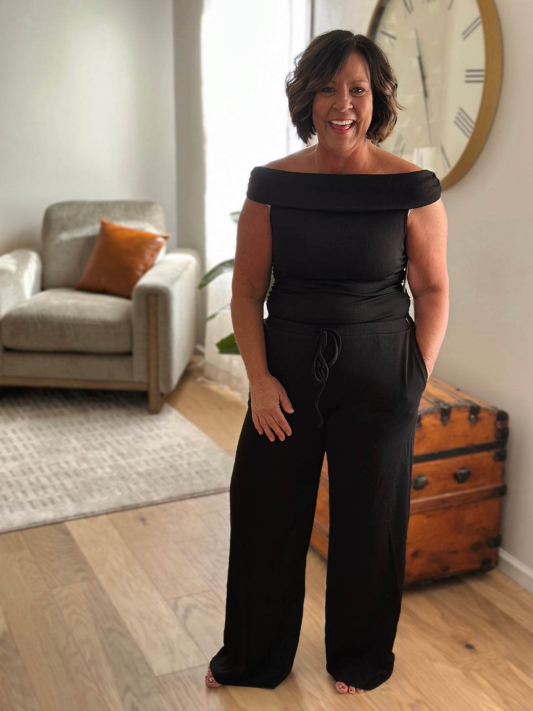 Woman wearing a black off-shoulder set standing in a living room.