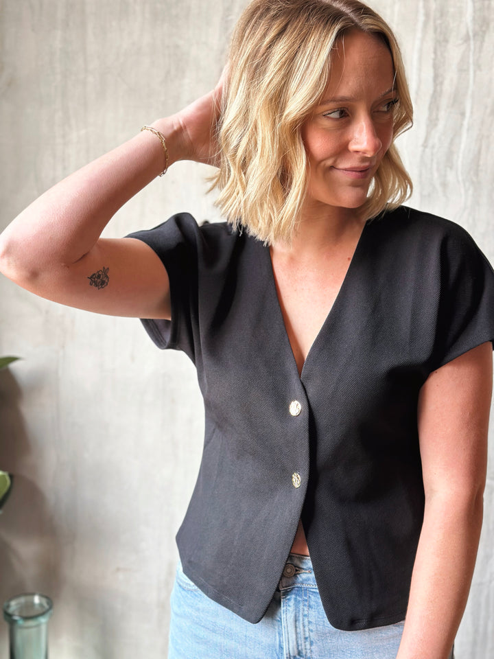 Woman wearing a black blouse with a V-neck and short sleeves against a neutral background