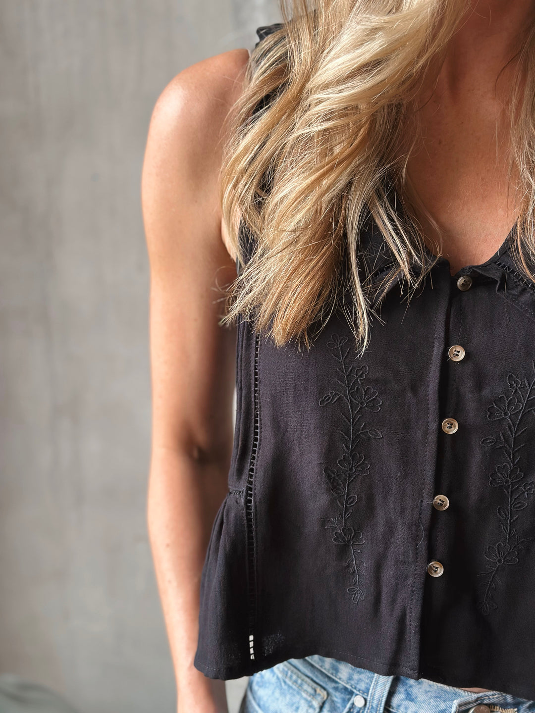 Black sleeveless top with intricate detailing worn by a person against a neutral background.