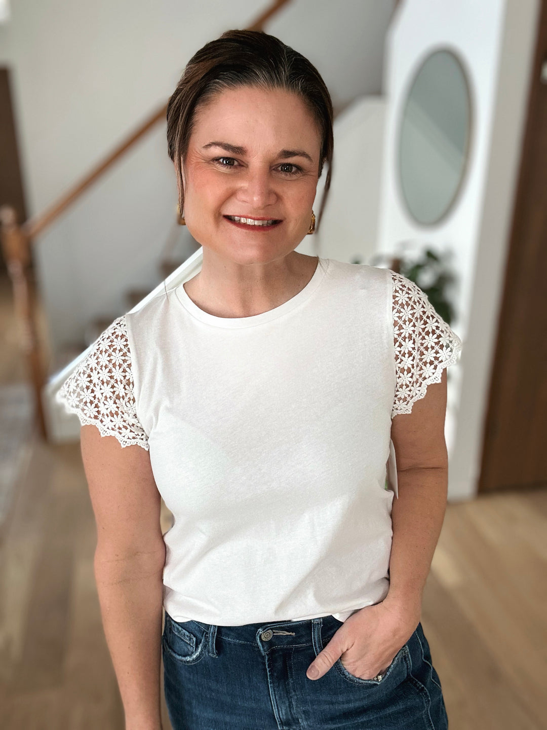 Woman wearing a white t-shirt with lace sleeves and blue jeans indoors.
