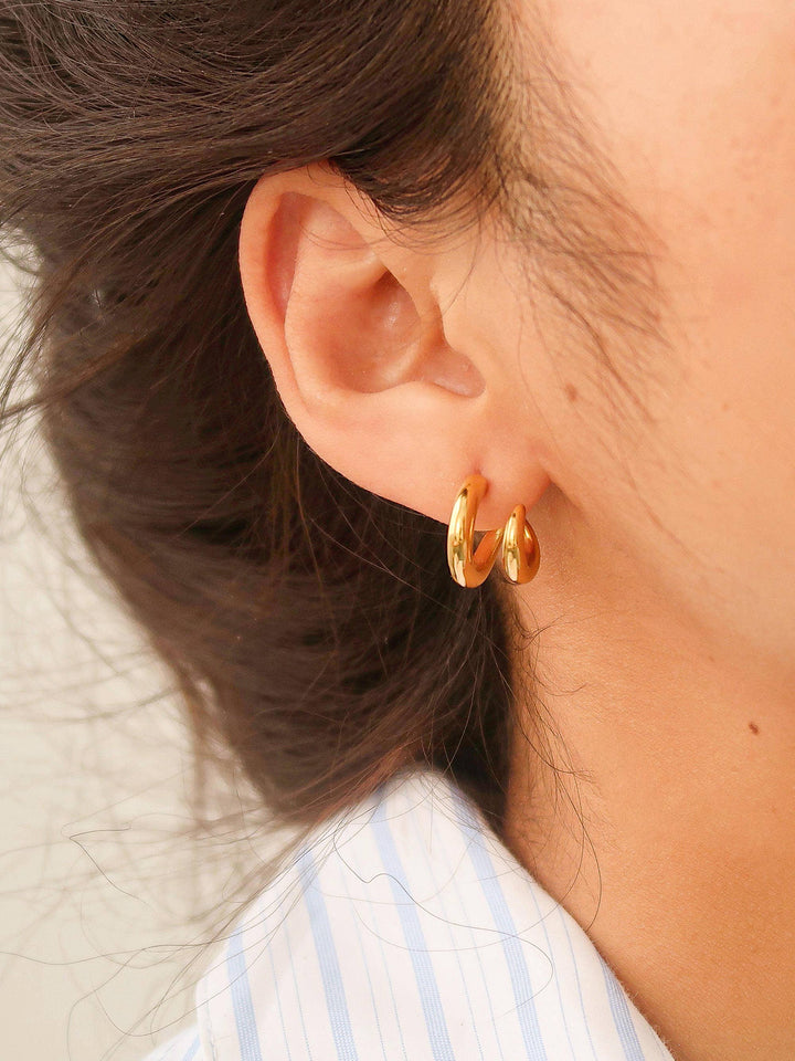 Close-up of an ear wearing gold hoop earrings with a blurred background