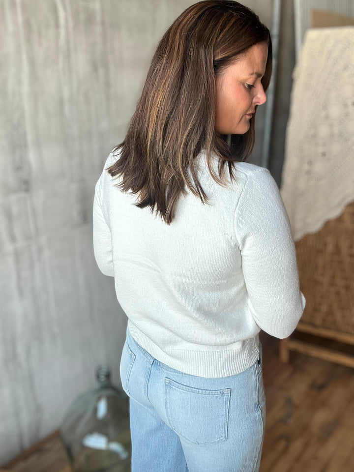 A woman is shown from the back wearing a white knit sweater and light blue jeans in an indoor setting.