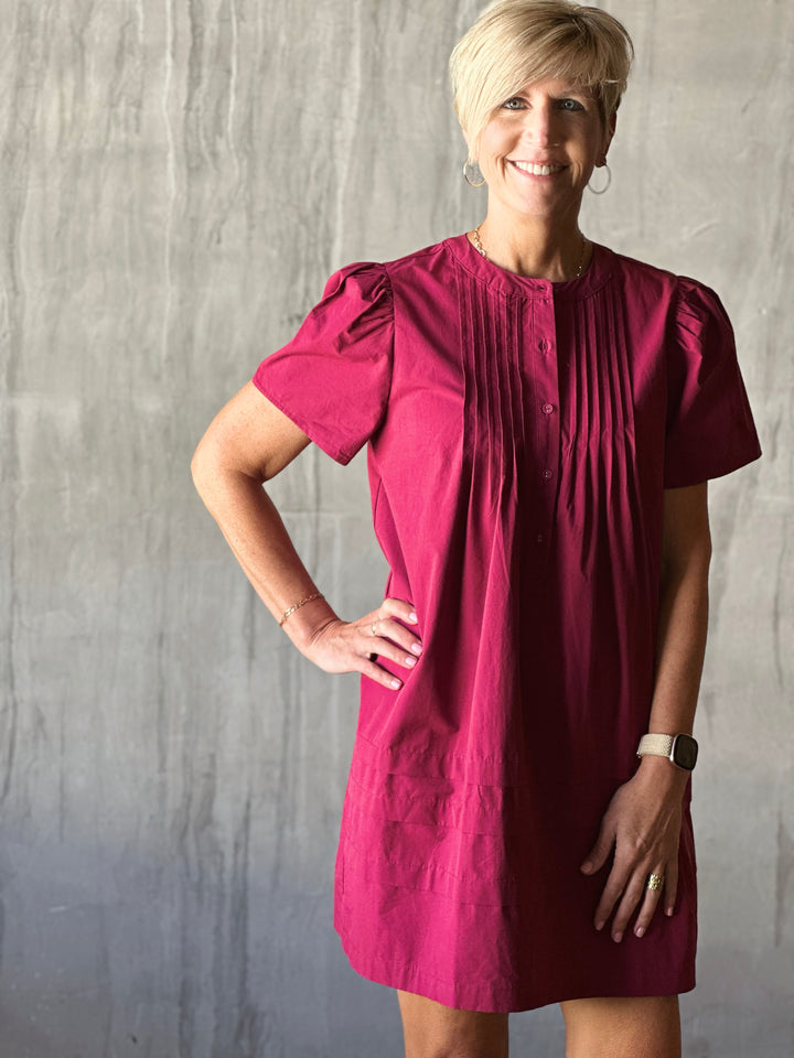 Front view of mini dress features a flattering pleated bodice and voluminous poplin puff sleeves. Deep Plum. 