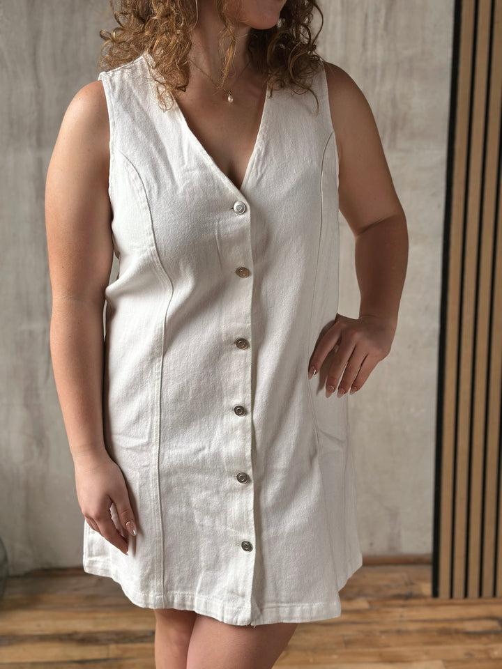 Woman wearing a white sleeveless dress with buttons against a neutral background