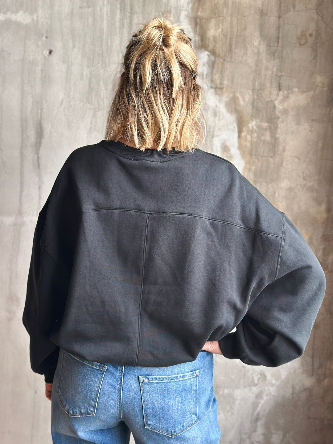 Person wearing a black jacket and blue jeans against a textured wall.
