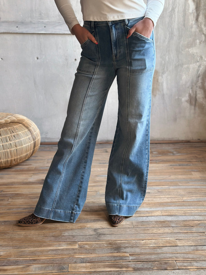 A person wearing blue flared jeans with a seam down the middle of the pants legs.