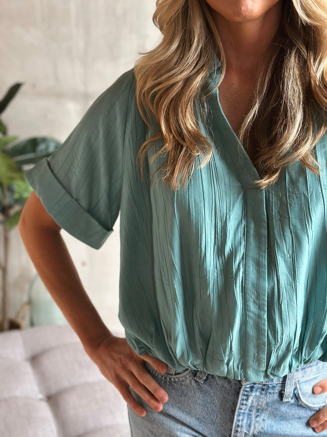 Person wearing a teal blouse with a blurred background.
