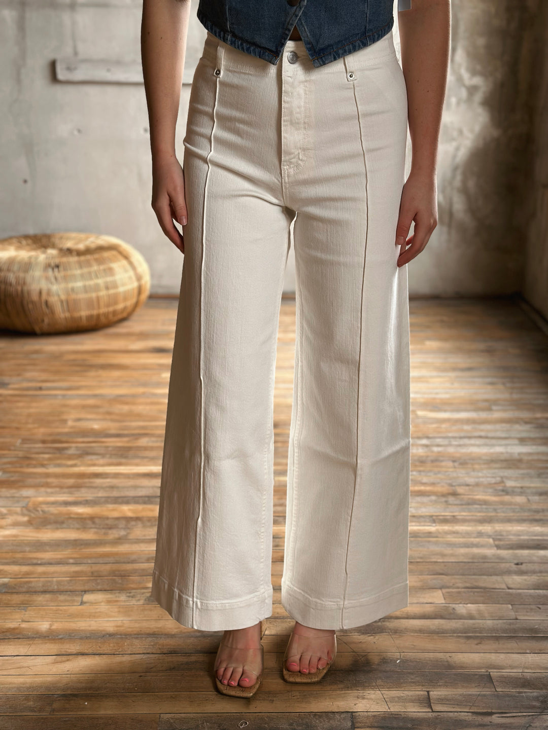 Person wearing white wide-leg jeans in a room with wooden floor and textured walls.