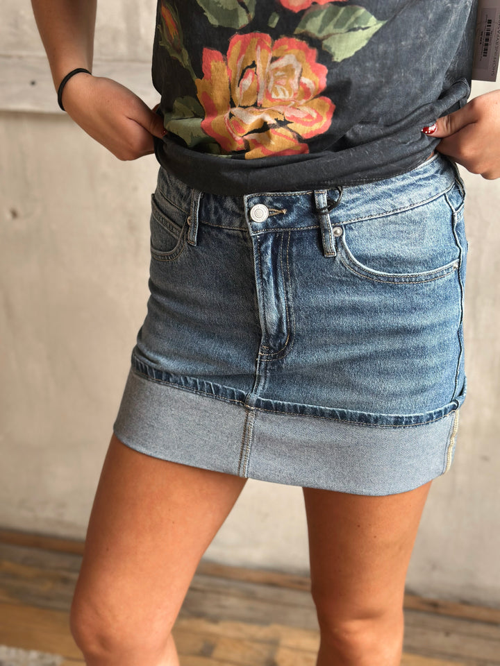 Person wearing a floral top and denim skirt against a neutral background.