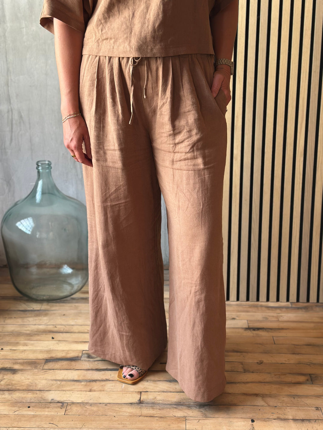 Person wearing brown pants standing in a room with wooden floor and glass container.