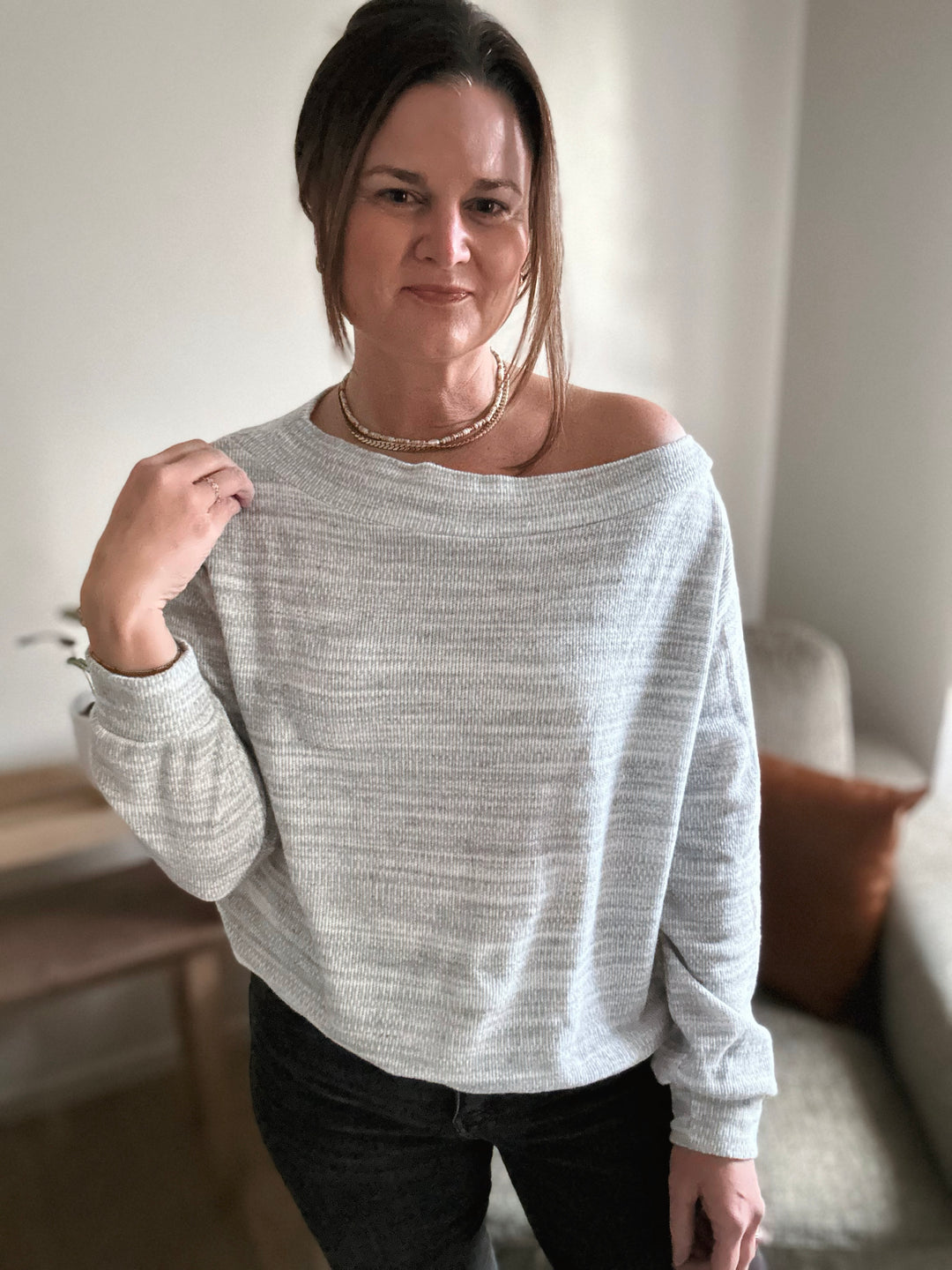 Woman wearing a light gray off-shoulder sweater indoors.