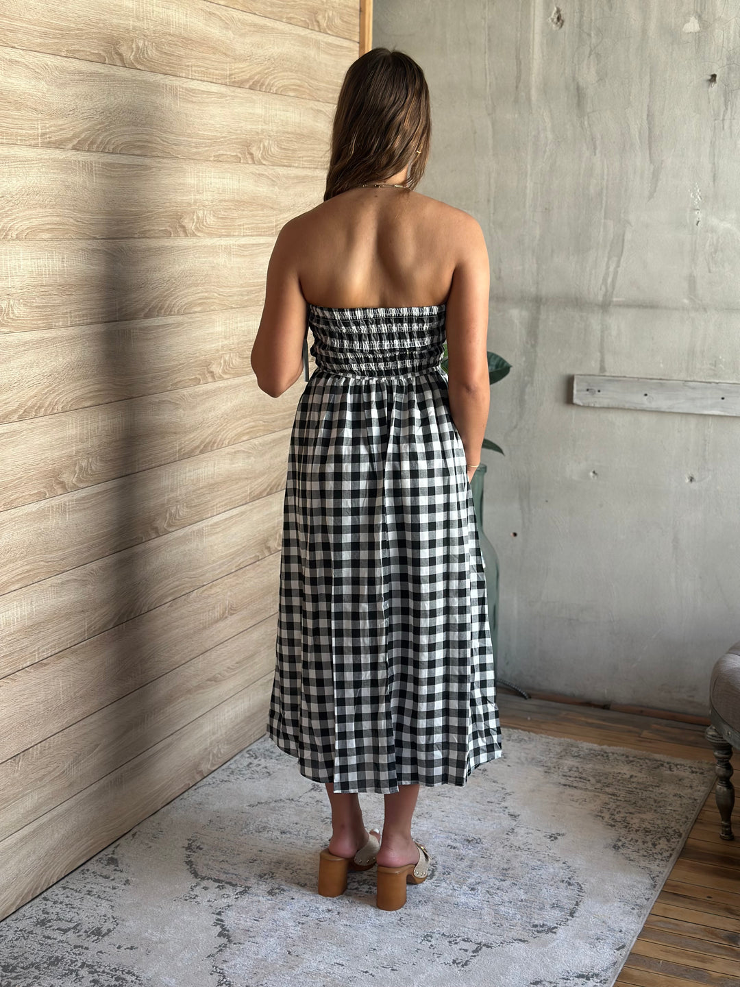 Woman wearing a black and white plaid and strapless dress standing in a room with wooden walls.