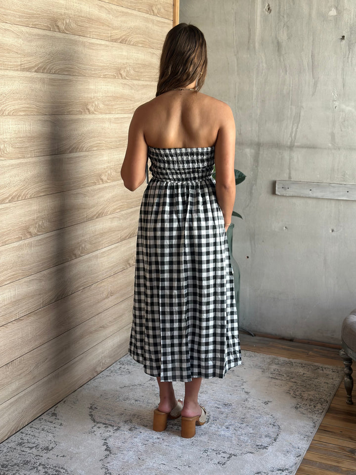 Woman wearing a black and white plaid and strapless dress standing in a room with wooden walls.