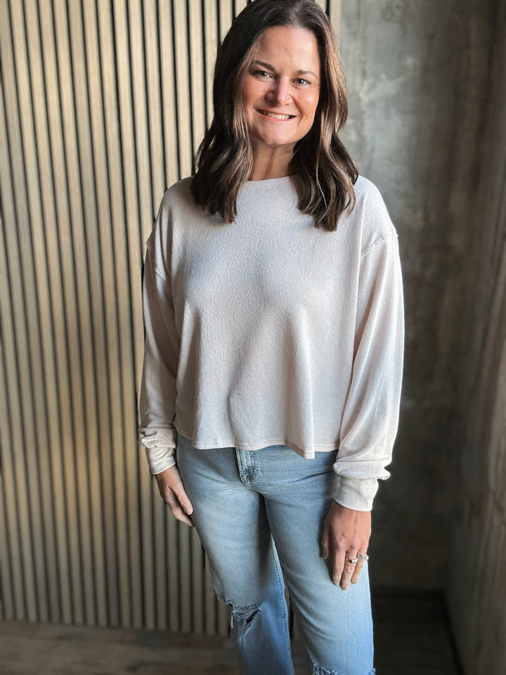 Woman wearing a light gray sweater and blue jeans against a textured wall.