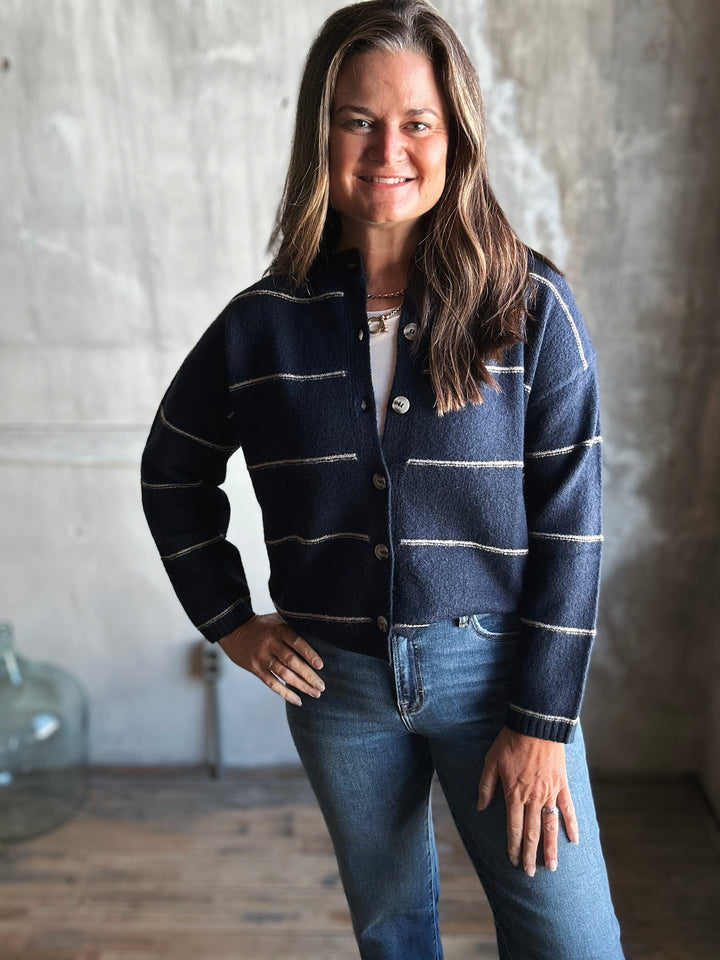 Woman wearing a navy striped cardigan and jeans against a textured wall.