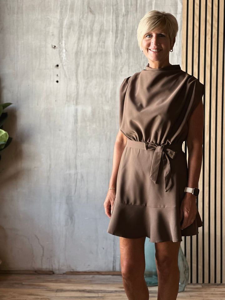 Woman wearing a brown dress standing against a textured wall.