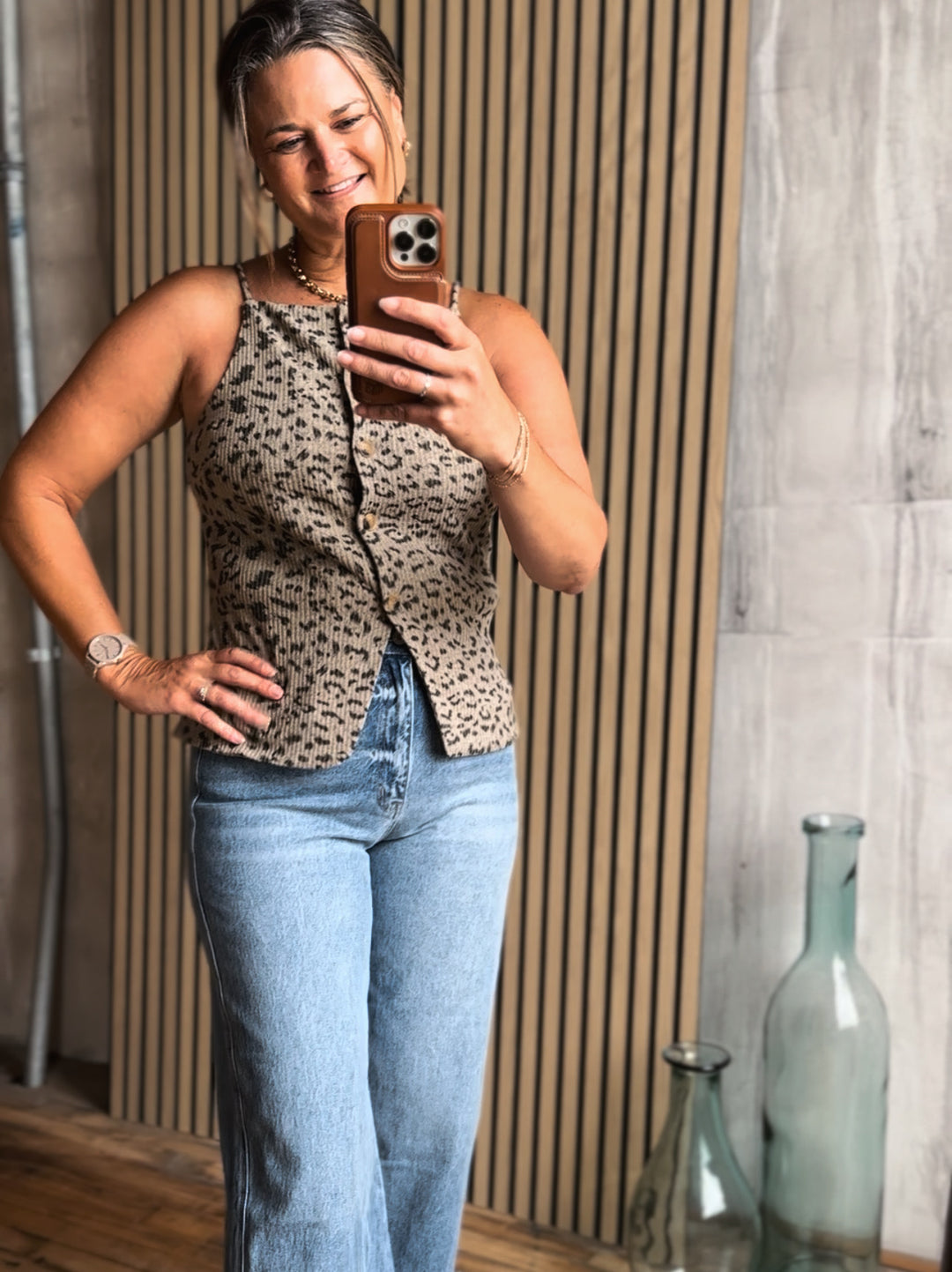 Woman taking a mirror selfie wearing a leopard print top and blue jeans.