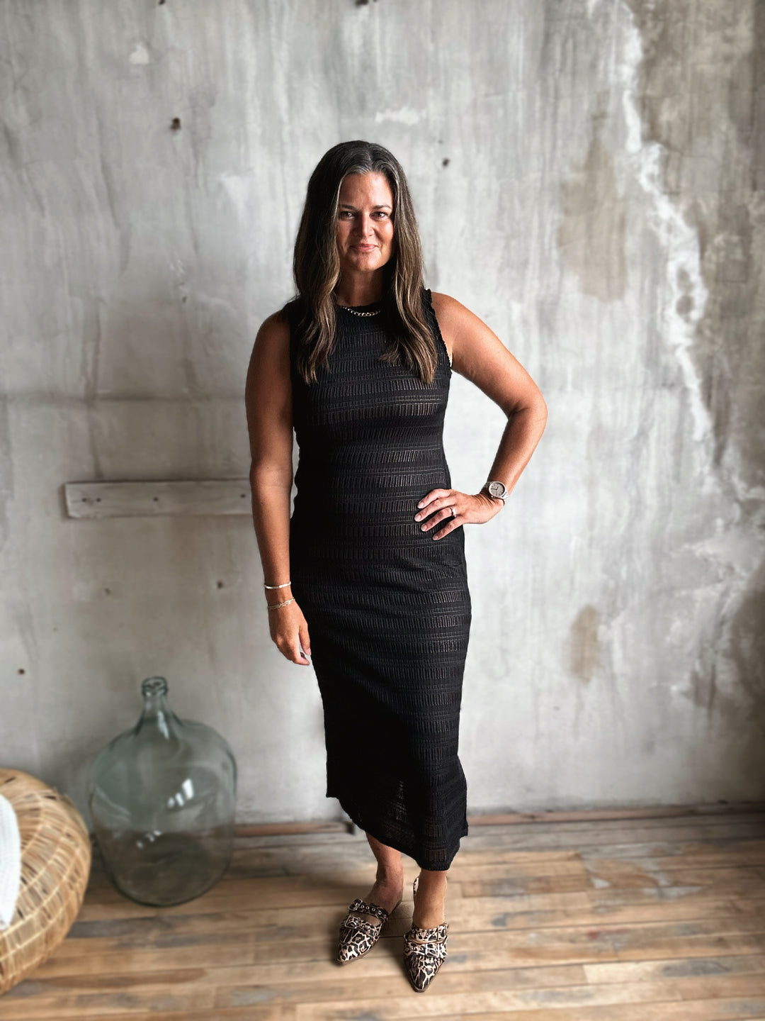 Woman in a black dress standing against a textured wall.