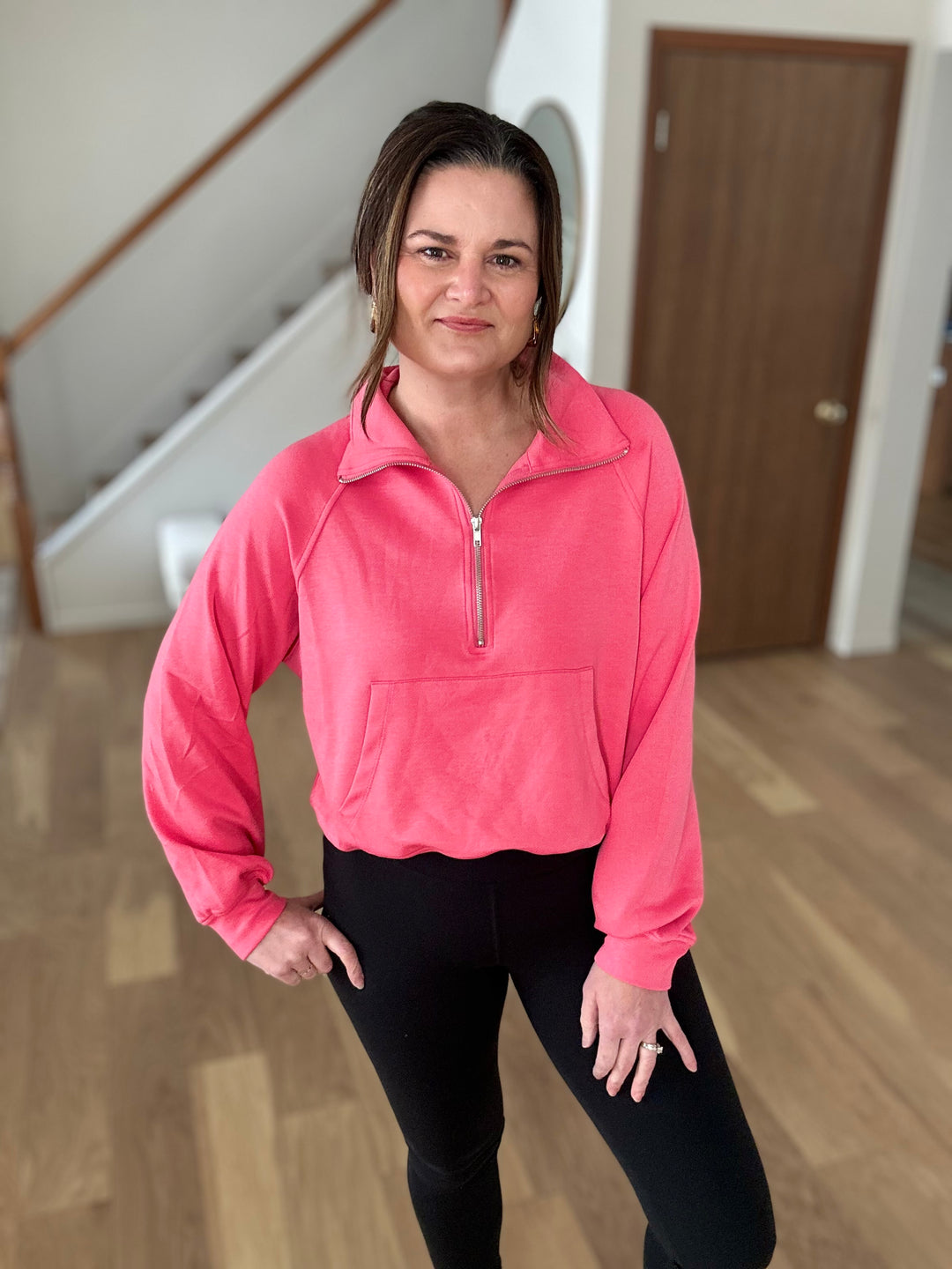 Woman wearing a pink pullover and black leggings indoors.