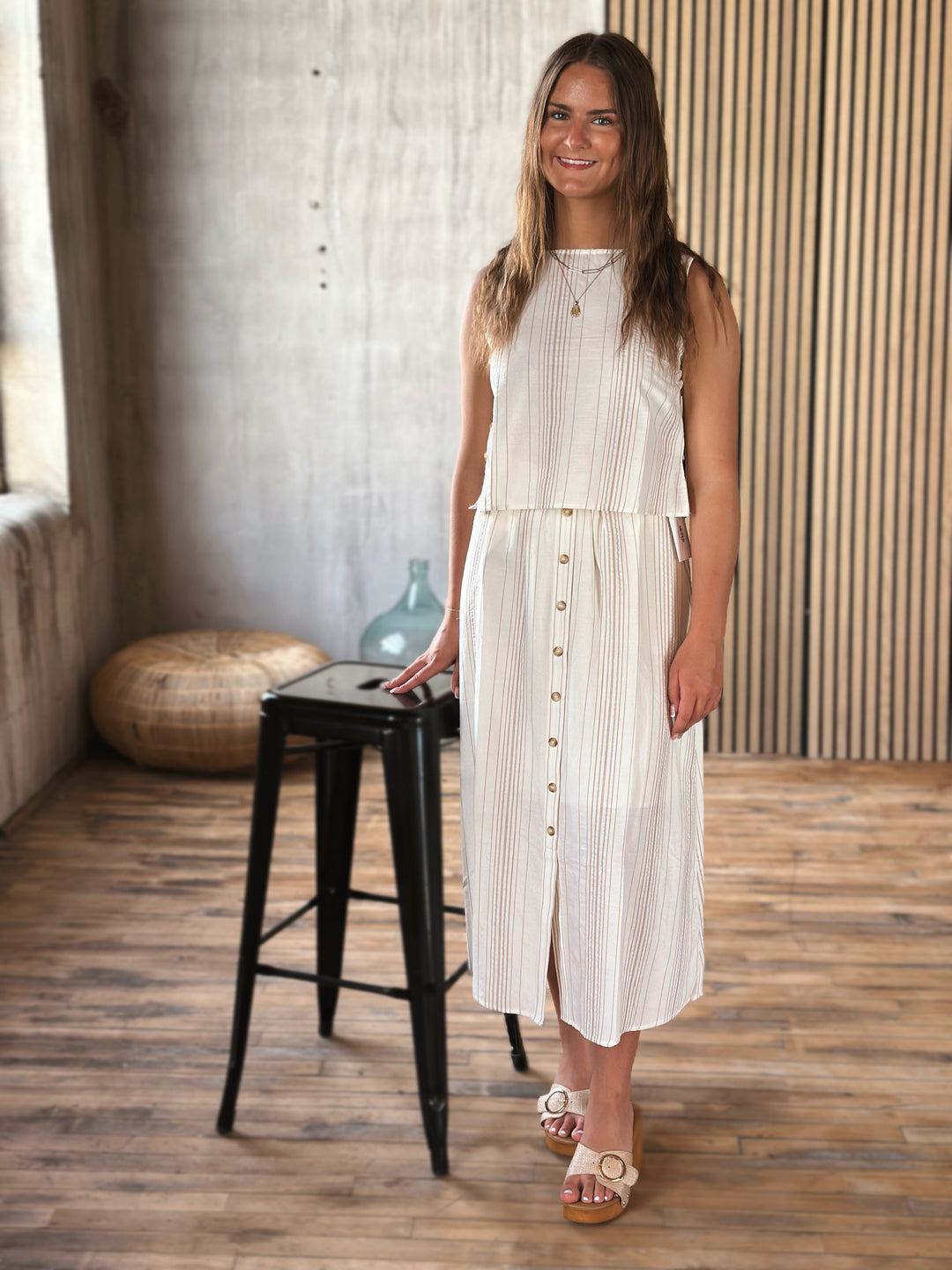 Woman in a white and beige outfit  standing in a room with a wooden floor and striped wall.