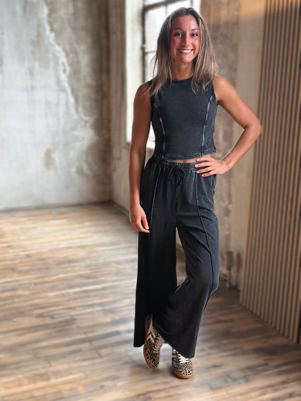 Woman wearing a black sleeveless top and wide-leg pants in an indoor setting.
