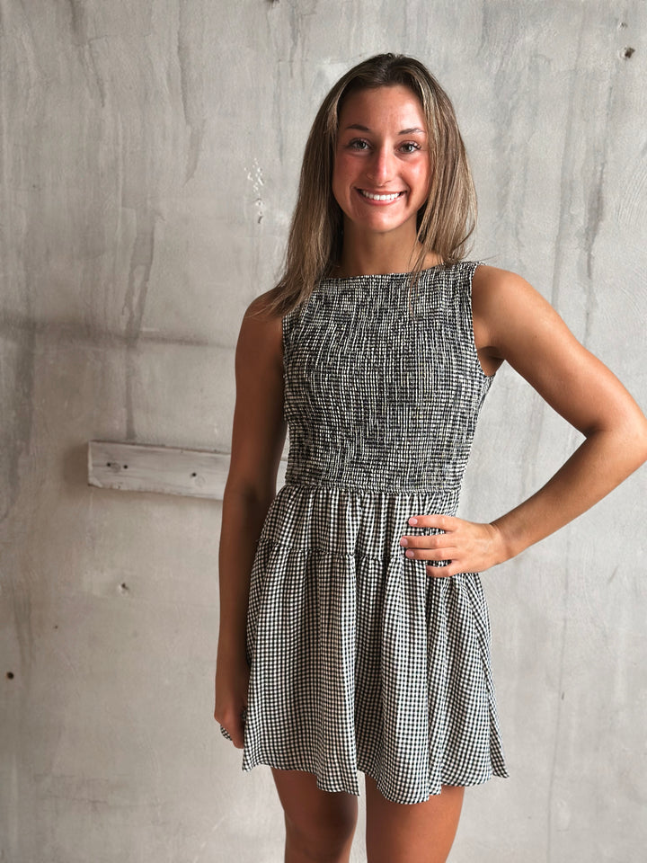 Woman wearing a black and white gingham dress against a gray concrete wall.