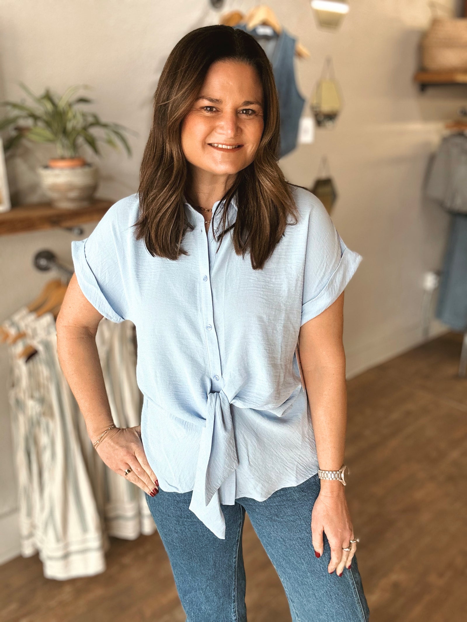Woman wearing a light blue shirt with a tie detail in a clothing store.
