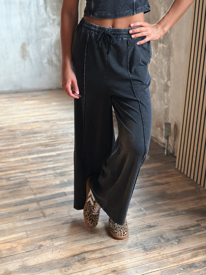 Person wearing black wide-leg pants and leopard print shoes in a room with wooden flooring and a striped wall.